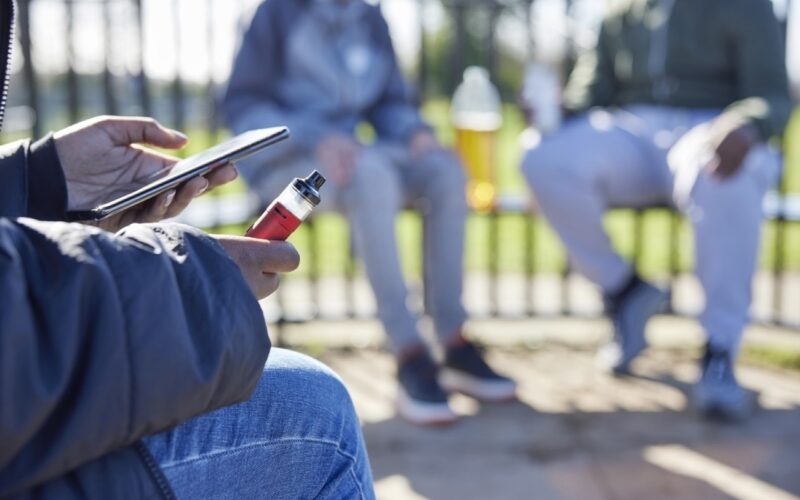 Teen holding a vape outdoors, used for coverage of the UK consultation on vape packaging, flavour names and retail display rules