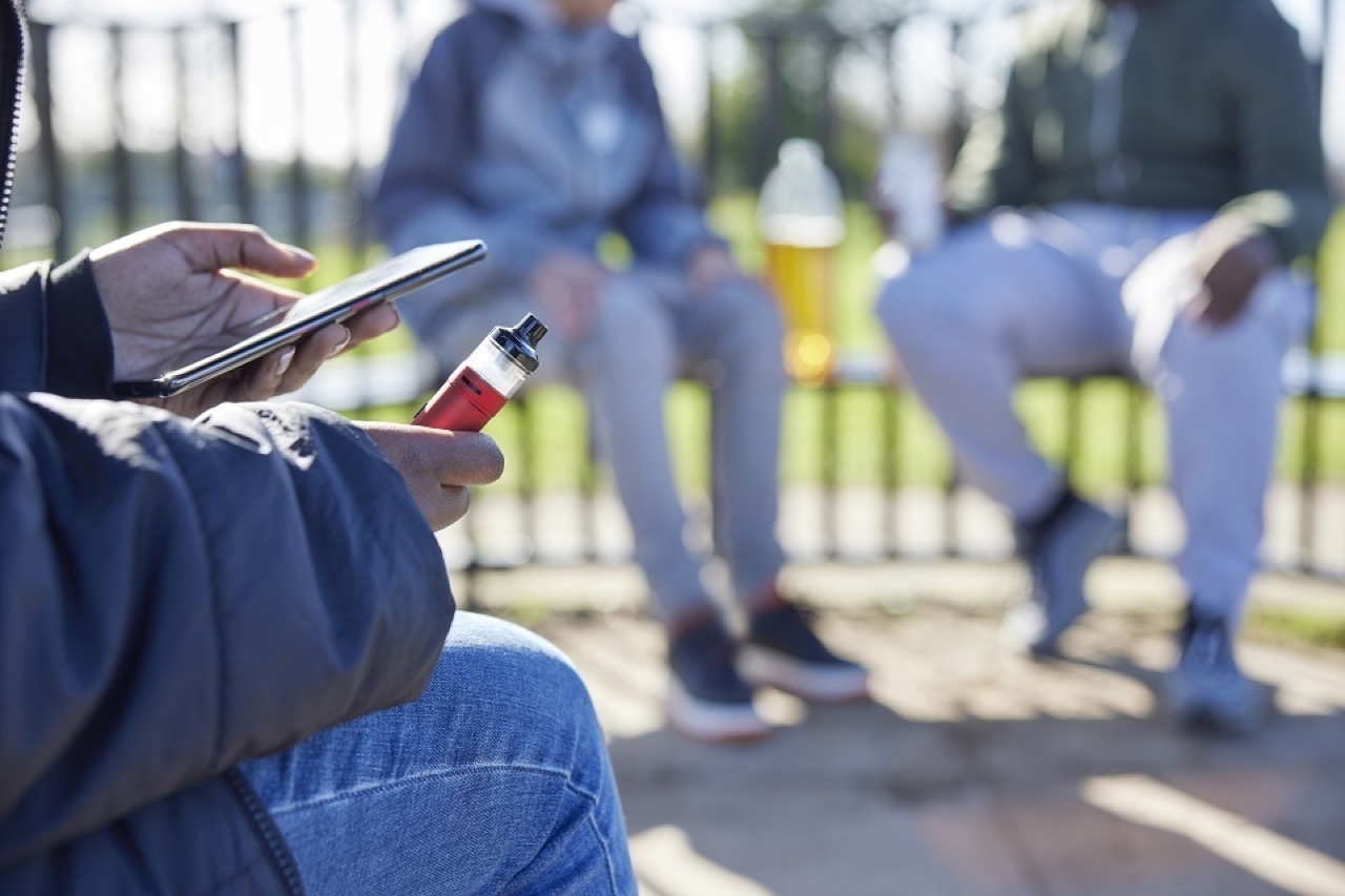 Teen holding a vape outdoors, used for coverage of the UK consultation on vape packaging, flavour names and retail display rules